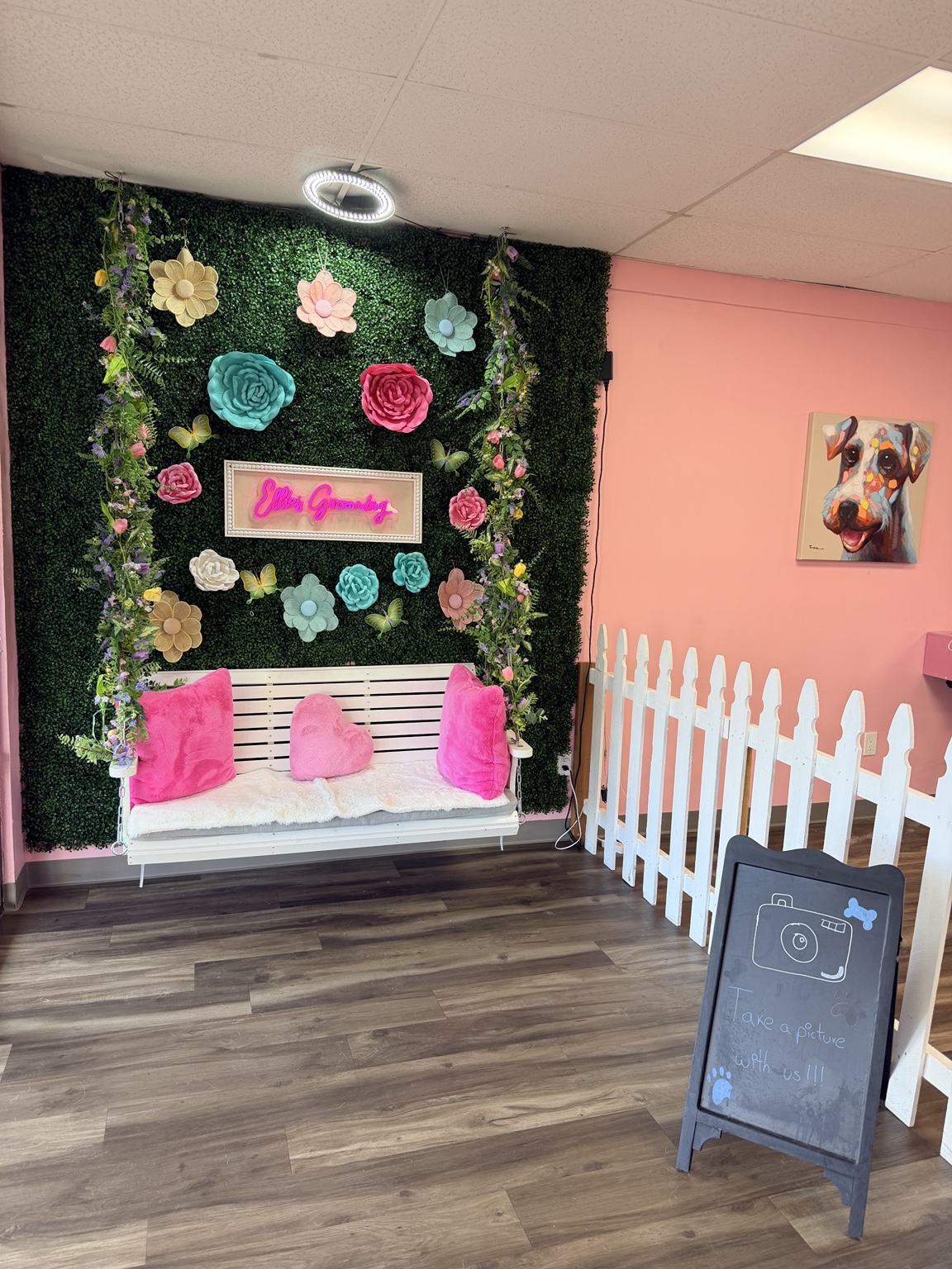 Ellie’s Grooming floral photo wall with a white swing, pink cushions, and neon sign